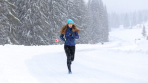 A young woman is running in bad weather on snowy trails.