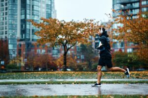 An Asian man is cold weather running in rain in autumn in a city with could sky in the background and rain coming down