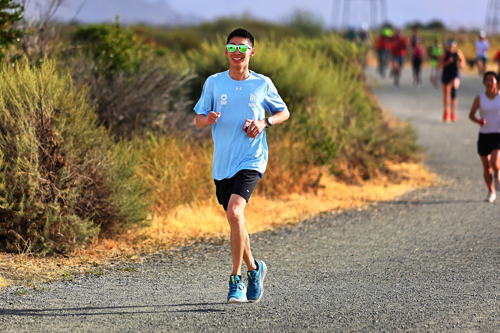 Eric He running on a sunny trail wearing sunglasses and a light blue shirt