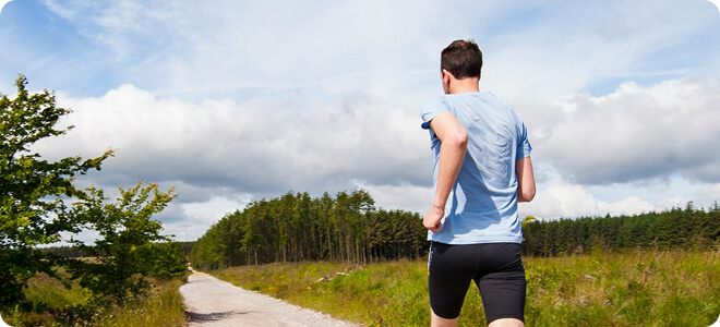 Man running down a path in an open field with trees in the background
